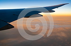 Wing of plane over white clouds. Airplane flying on sunrise sky. Scenic view from airplane window. Commercial airline flight.