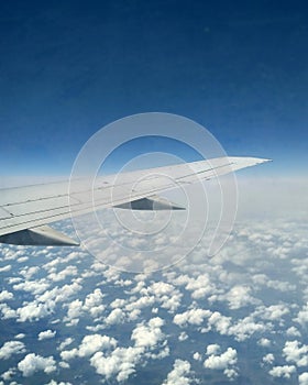 Wing of the plane in the sky with small clouds. View from the airplane`s window.