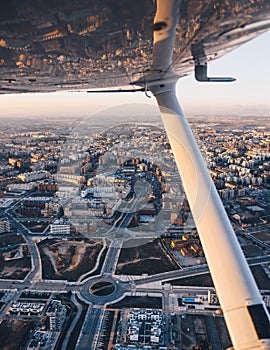 Wing view of a small plane flying at sunset over the city.