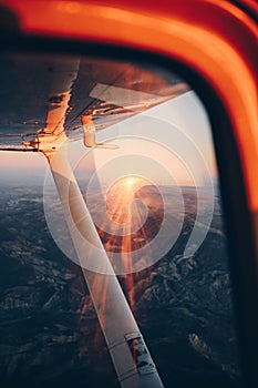 Wing view of a small plane flying at sunset over the city and the sea shore