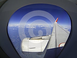 wings of airplane during the flight look from the passenger window. There are white clouds in the blue sky