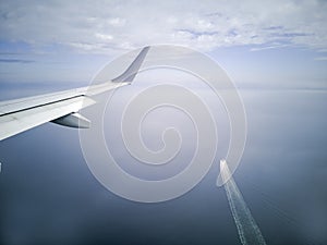 Wings of the plane during the flight look from the passenger window. There are not many white clouds in the blue sky above the gro