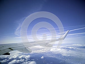 The wings of the plane during the flight look from the passenger window. There are white clouds in the blue sky