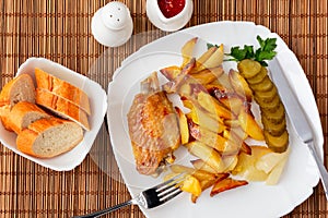 Wings of turkey baked with potato pieces on a white plate worth a bamboo napkin with tartar sauce and tomato sauce and