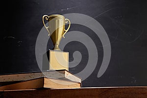 wining trophy on stack of book against blackboard