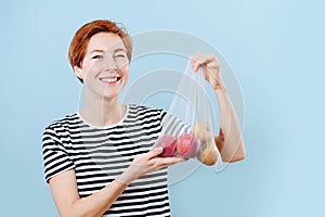 Winking cheerful woman showing apples in a net bag