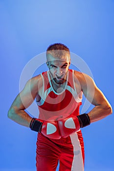 Winner emotions. Male boxer in red uniform and boxing gloves training isolated on blue background in neon. Strength