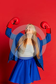 Winner emotions. Young business woman or happy student wearing blue suit and red boxing gloves over bright red