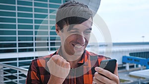 Winner smiling young male looking at his smartphone screen and celebrate good news victory success. Standing near the
