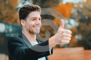 Winner. Success. Brunette young man in business clothing in office district smiles to camera and gives thumbs up. Happy