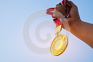 Winners Champion in success award concept : Woman hands raised holding gold medals with ribbon against blue sky background to show