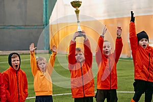 Winners. Group of little boys, children in uniform, football players raising award, trophy. Kids training on outdoor