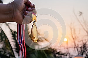 Winners success award concept. Silhouette woman hands raised and holding gold medals with Thai ribbon against sunset light sky