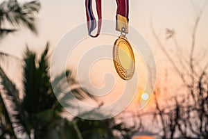 Winners success award concept. Silhouette woman hands raised and holding gold medals with Thai ribbon against sunset light sky