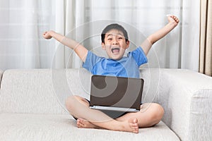 Winning Asian Chinese little boy using laptop on the sofa