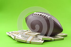 Winning bet on sporting event, money in sport and sports betting conceptual idea with american football ball and wads of cash