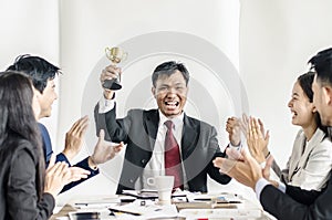 Winning business team with a man executive holding a gold trophy .