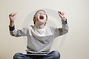 Winning a game. Happy boy screeming euphoric sitting with digital tablet computer.