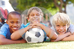 A winning team of best friends. Three happy boys lying outside in the sun with their soccerball - copyspace.