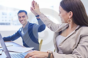 Winning throughout the day with teamwork. two businesspeople giving each other a high five while working in an office.
