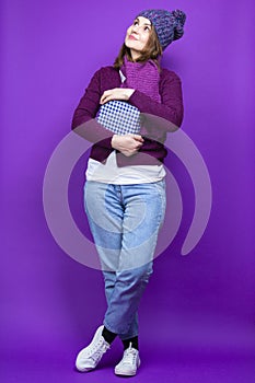 Winsome Adult Caucasian Female Woman in Warm Knitted Hat and Purple Scarf Posing with Big Wrapped Giftbox Present And Smiling