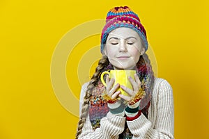 Winsome Calm Caucasian Teenage Girl in Warm Seasonal Hat and Knitted Scarf Holding Big Yellow Cup While Drinking tea or Coffee