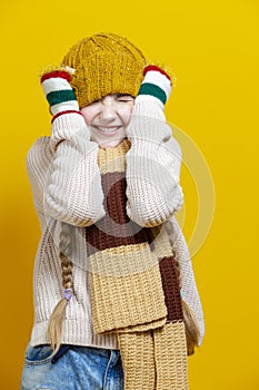 Winsome Exclaiming Caucasian Blond Girl In Warm Knitted Hat and Scarf Posing with Lifted Hands While Making Faces And Pulling Hat