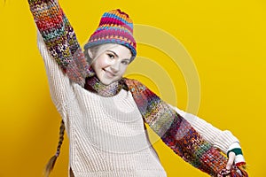 Winsome Exclaiming Caucasian Blond Girl In Warm Knitted Hat and Scarf Posing with Lifted Hands While Pulling Scarf To Sides
