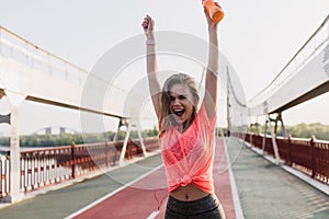 Winsome female runner enjoying victory. Outdoor portrait of slim gorgeous woman posing with hands u