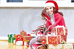 Winsome Smiling Red-Haired Cucasian Santa Girl With a Bunch of Gift Boxes Speaking by Cellphone Indoors. Sitting Under the Plaid