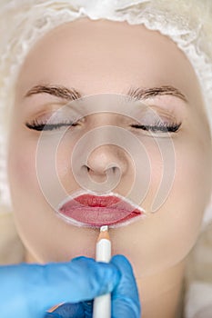 Winsome woman Having Permanent Lips Makeup at Beauty Salon During Permanent Makeup Tattoo While Drawing Contour with a white lip