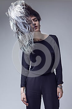 Winsome Young Caucasian Girl With Colorful Hair Style in Black Shirt Posing With Flyaway hair With Eyes Closed Over Gray