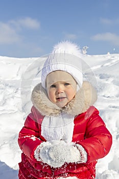 Winter activities for children. A little girl is trying to make a snowball. She is dressed in a bright red coat with a white hat