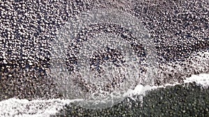 winter aerial flight top over waves rolling on artic ocean shore with round stones, ocean waves at storm