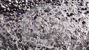 winter aerial flight top over waves rolling on artic ocean shore with round stones, ocean waves at storm