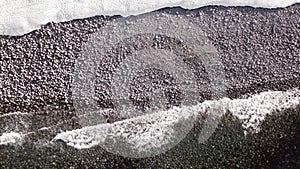 winter aerial flight top over waves rolling on artic ocean shore with round stones, ocean waves at storm