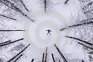 Winter aerial top view of man with blue jacket in the coniferous mountain forest. Spruce forest covered with snow. Man is lying in