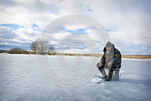 In the winter afternoon, a man sits on the river fishing, he caught a roach