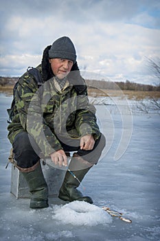 In the winter afternoon, a man sits on the river fishing, he caught a roach