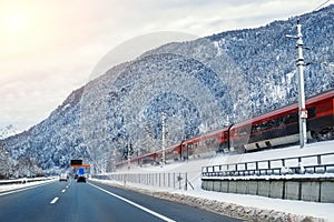 Winter alpine mountain highway and parallel railway road with intercity fast train and blue sky on background at bright cold sunny