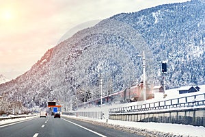 Winter alpine mountain highway and parallel railway road with intercity fast train and cloude sunset sky on background at cold day