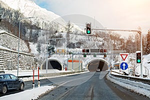 Winter alpine road landscape with tunnel, forest, mountains and blue sky on background at bright cold sunny day. Car