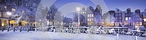 Winter in Amsterdam with snow. Panorama with bicycles, bridge, canal, old houses at night