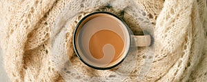 Winter and autumn hot drink. Hot chocolate or cocoa wrapped in woolen soft warming scarf on gray background. Seasonal concept,