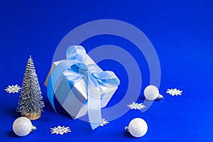 Winter background blue. White gift box with blue ribbon, winter tree, Snowflakes and Silver balls in Christmas composition on blue