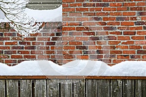 Winter background, falling snow and piles of snow on a fence railing with a brick chimney in the background