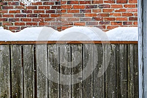 Winter background, falling snow and piles of snow on a fence railing with a brick chimney in the background