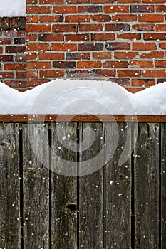 Winter background, falling snow and piles of snow on a fence railing with a brick chimney in the background