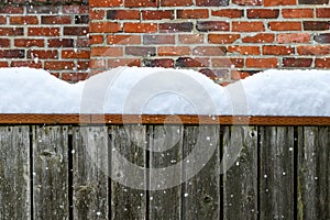 Winter background, falling snow and piles of snow on a fence railing with a brick chimney in the background