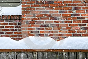 Winter background, falling snow and piles of snow on a fence railing with a brick chimney in the background